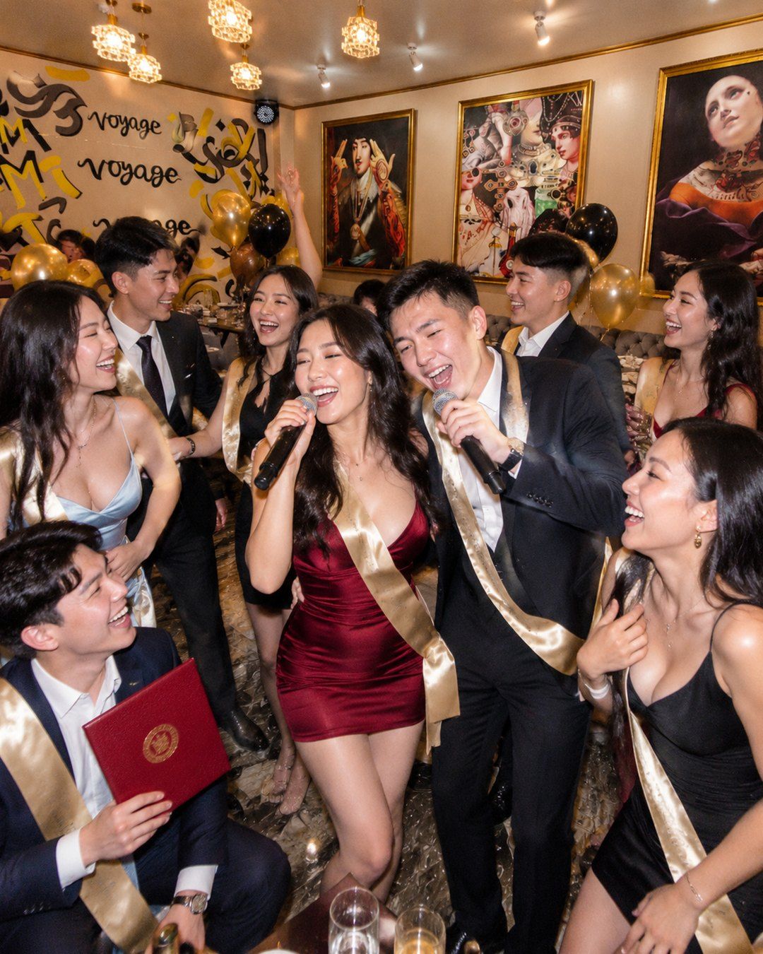 Graduation in an RMM room: graduates in evening dresses and suits sing and hug, one holds a red diploma